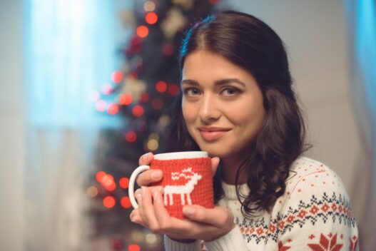 Kvinde i juletrøje med en varm kop kaffe i hånden